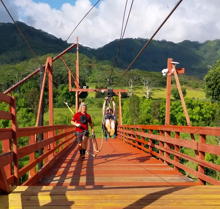 A guide on a red wooden bridge between platforms as a rider zips overhead