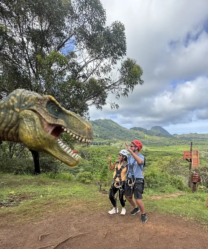 Guests posing beside a dinosaur statue above the reservoir
