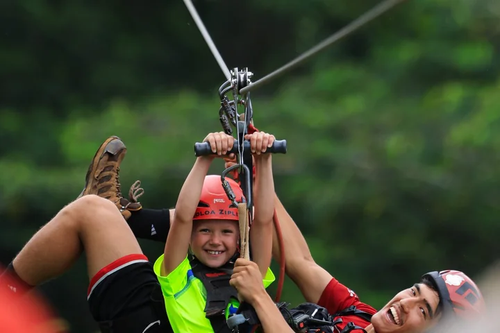 A young rider on a zipline trolley with an adult alongside